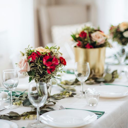 A bright dining table set with glassware and a floral centerpiece of red and peach roses, for a special celebration.